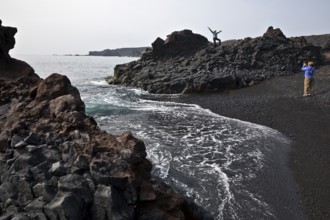 On the black lava beach Djúpalónssandur with young female tourists photographing and posing,