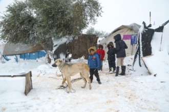 Displaced Syrian children playing in the snow near their tents inside a refugee camp during winter.