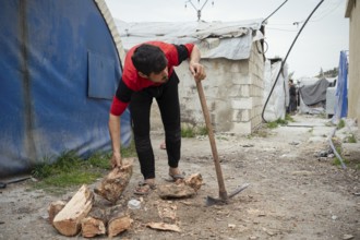 A young displaced Syrian man cutting firewood to use for heating inside a refugee camp. Aleppo,