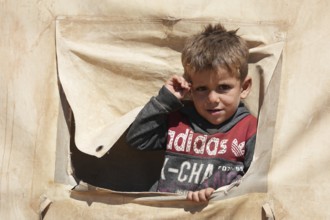 A portrait of a sweet Syrian girl looking through a peephole in a makeshift refugee tent. Aleppo,