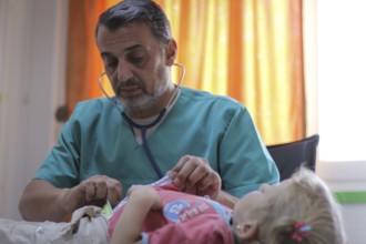 A doctor examining a displaced Syrian child inside a mobile clinic at a refugee camp. Aleppo, Syria