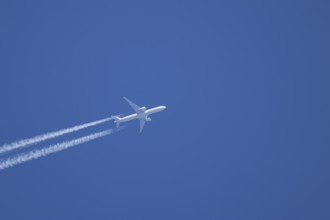 Jet passenger aircraft with a vapour trail or contrail flying in a blue sky, England, United