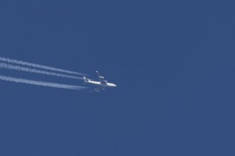 Boeing 747 jumbo jet cargo aircraft with a vapour trail or contrail flying in a blue sky, England,