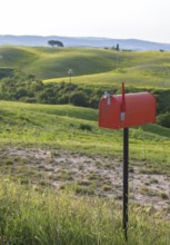 Red standing letterbox in a field with lush green hills in the background, Tuscany, Italy