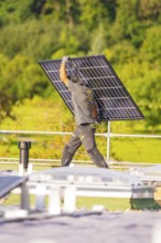 Person carrying a solar panel on a green roof, PV installation, commercial customers, new building,