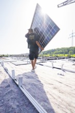 Workers carrying a solar panel on a roof in sunny weather, PV installation, commercial customers,