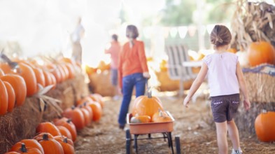 Two young girls pulling their pumpkins in A wagon at a pumpkin patch on a fall day
