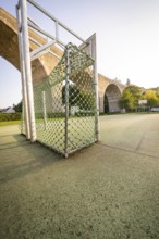 Sports goal with net on an asphalt pitch under a large bridge and trees, Nagold, Calw district,