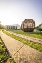 Wooden sculpture next to a modern building in the sunshine on a green lawn, Nagold, district of