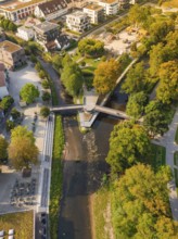 River with bridge in an urban park, surrounded by autumnal trees and buildings, Nagold, district of