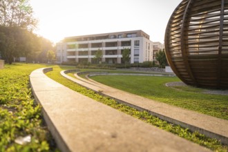 Modern park landscape with curved paths and a large building in the evening light, Nagold, district