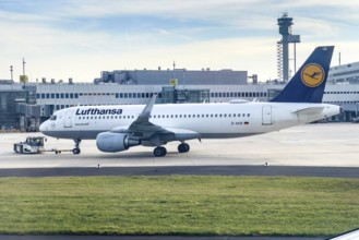Lufthansa Airbus A320-200 being towed by a tug on the apron, in the background terminal and modern