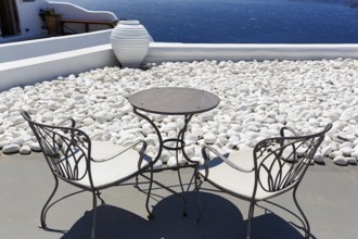 White gravelled area, wrought-iron table and two chairs, vase on a terrace by the sea, Oia,