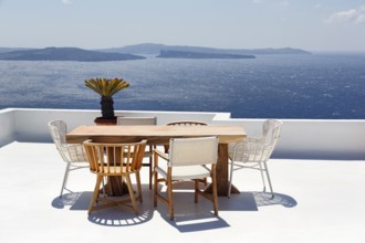 Wooden table and various chairs on a white terrace by the sea, view of the caldera, Oia, Santorini,