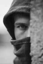 Mann in Kapuzenpullover schaut mit intensivem Blick hinter einer Mauer und beobachtet eine