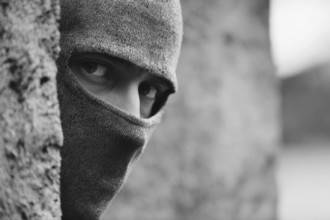 Mann in Kapuzenpullover schaut mit intensivem Blick hinter einer Mauer und beobachtet eine