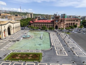 A large square with a fountain surrounded by impressive buildings under a clear sky, aerial view,