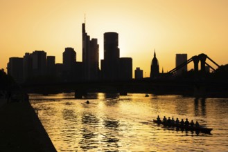 A rowing boat navigates the Main as the sun sets behind the Frankfurt banking skyline, Frankfurt am