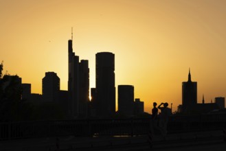 Two men cross the rafter bridge over the Main in the evening as the sun sets behind the Frankfurt