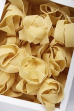 Raw pappardelle pasta, pasta nests, in a paper box, top view, no people