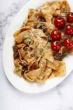 Pappardelle pasta with bolognese sauce, topped with parmesan cheese and cherry branch, homemade, no