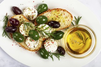 A plate with a snack, ciabatta bread with cheese and olives, olive oil, spices and herbs, top view,
