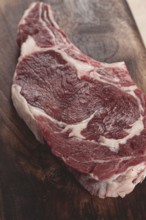 Raw rib eye steak, cowboy steak, wooden chopping board, marble table, top view, no people