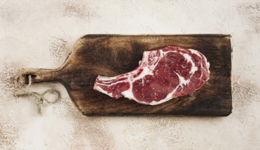 Raw rib eye steak, cowboy steak, wooden chopping board, marble table, top view, no people