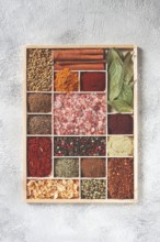 An assortment of spices laid out on a wooden tray, arranged in wooden compartments, top view