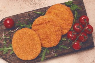Crispy fried fish cutlets, fish burgers, on a wooden chopping board, with arugula and cherry