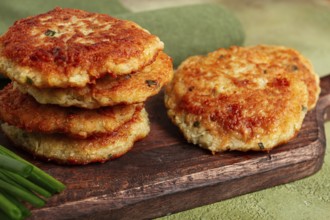 Crispy potato pancakes Latkes, stacked on a wooden board next to fresh green onions, natural light,