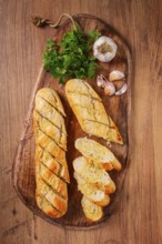 Garlic bread, baguette with garlic butter and herbs, on a wooden board, with herbs and garlic