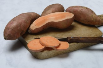 Sweet potatoes with kitchen knife on wooden board, Ipomoea batatas