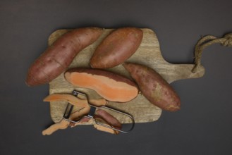 Sweet potatoes with potato peeler on wooden board, Ipomoea batatas