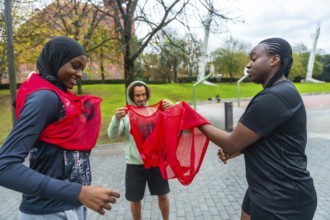 Diverse friends smiling and gearing up on an outdoor urban basketball court, putting on team bibs