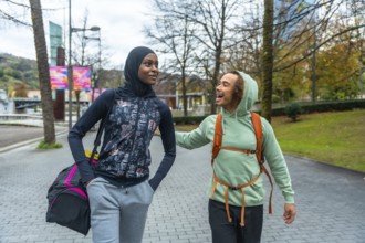 Diverse young adult friends wearing activewear walking and talking in an urban park, sharing a