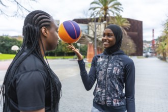 Two diverse young women enjoying a friendly basketball game at an outdoor court, one skillfully
