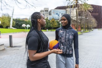 Diverse young women, one wearing a hijab and another with braids, talking and bonding while holding