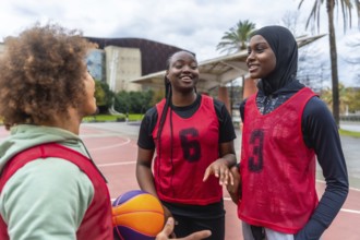 Three diverse young women, including one wearing a hijab, smiling and discussing before playing