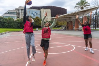 Diverse young friends actively competing in a street basketball game on an outdoor court, jumping