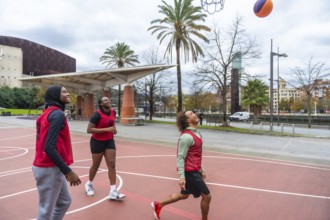Diverse group of young adult friends playing basketball on an urban court, with a woman wearing a