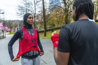 Young black woman wearing a hijab and training bib talking with a friend while preparing for her