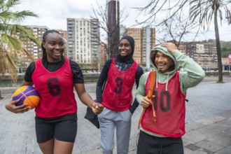 Three diverse friends, a young woman holding a basketball and two people wearing red bibs, walking