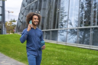 Smiling young Mixed-race man with curly hair walking confidently along a modern office building,
