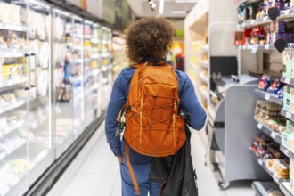 Person carrying a backpack walking down a grocery store aisle, navigating between refrigerated