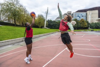 Young diverse friends are actively playing basketball on an outdoor court, a man jumping high