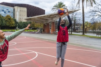 Woman in hijab smiling and shooting a basketball during a friendly game on an outdoor urban court,