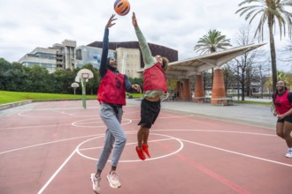 Diverse young women are jumping and reaching for a ball during a friendly outdoor basketball game