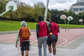Young diverse friends wearing sports bibs and carrying bags, walking united towards basketball