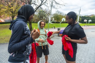 Diverse friends on an urban basketball court smiling and holding red pennants, preparing to play